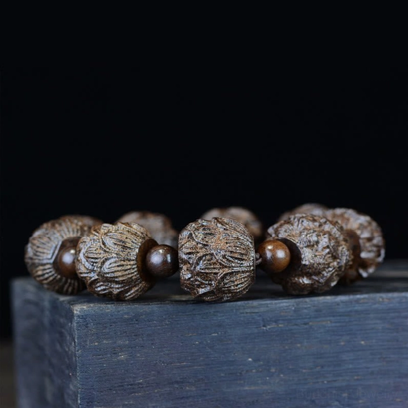 Ebony wood lotus bracelet displayed flat on dark wooden surface, showing complete 9-bead design with spacer beads arrangement