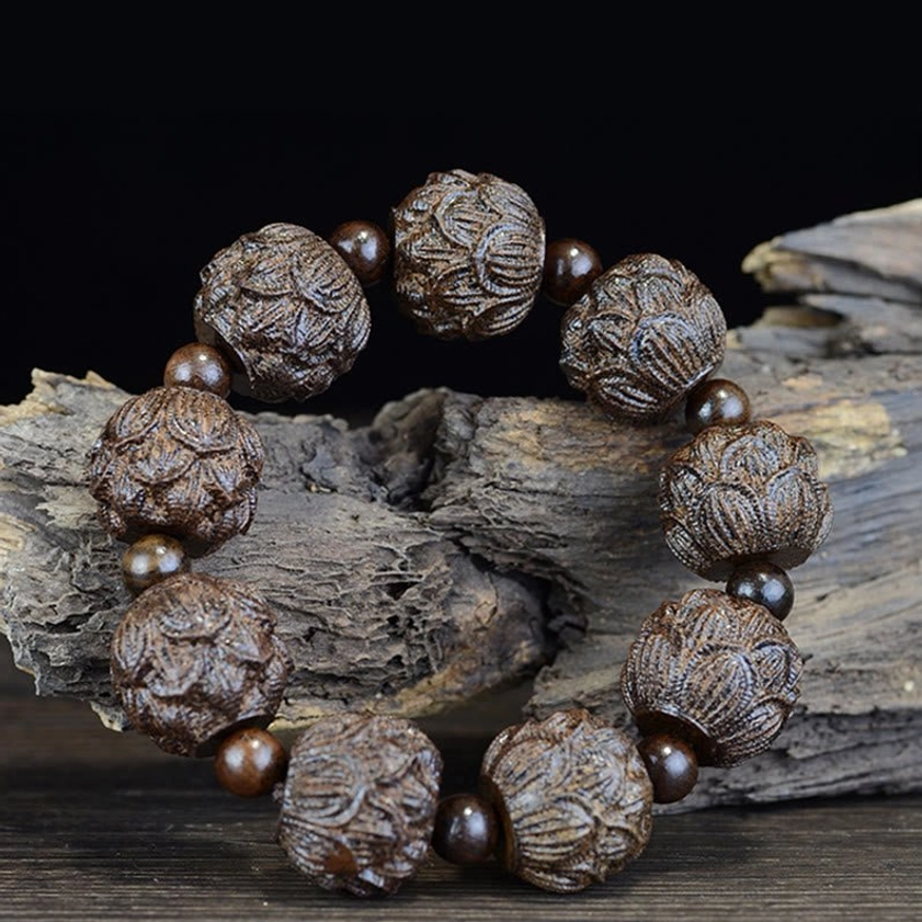 Dark ebony wood lotus carved bracelet on weathered dead wood background, oblique view highlighting three-dimensional bead carvings
