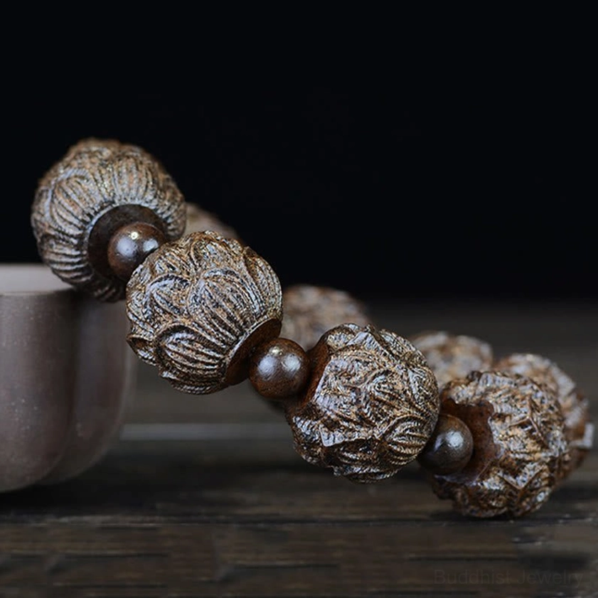 Lotus engraved ebony wood bracelet close-up side angle, showing detailed carving work next to ceramic cup on wooden table