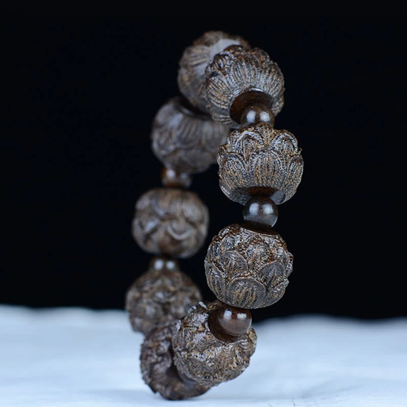 Ebony wood Buddhist lotus bracelet displayed vertically on white cloth, showing detailed lotus carvings and bracelet construction