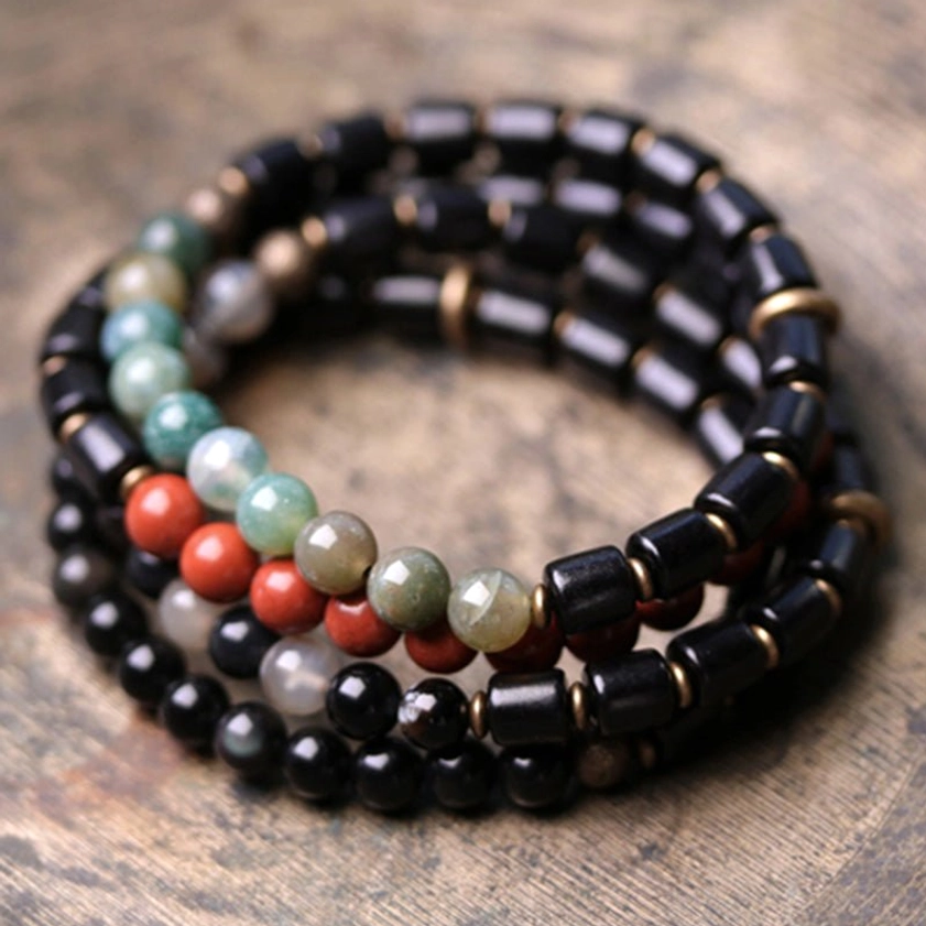 Triple strand coiled Buddhist bracelet with ebony wood, red jasper, moss agate and copper beads on rustic table