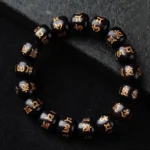 Om Mani Padme Hum ebony wood bracelet with golden Sanskrit engravings on barrel-shaped beads, overhead view on dark matte background