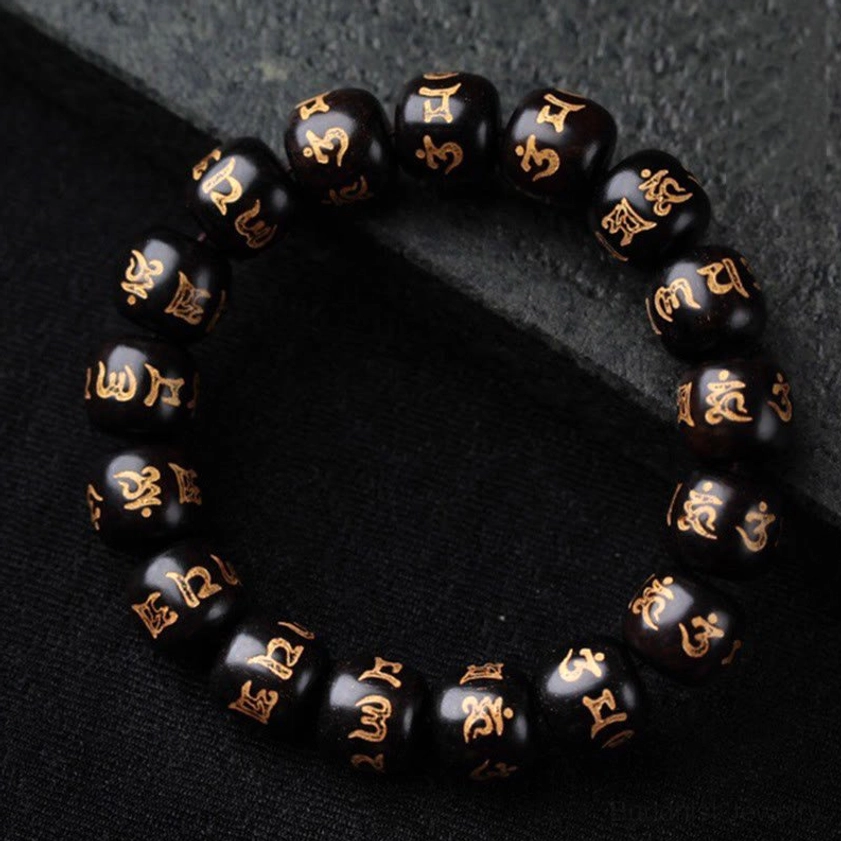 Om Mani Padme Hum ebony wood bracelet with golden Sanskrit engravings on barrel-shaped beads, overhead view on dark matte background
