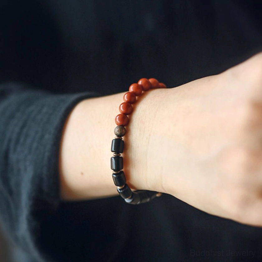 Close-up side view of ebony wood and red jasper Buddhist bracelets worn on wrist against dark clothing