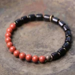 Ebony wood and red jasper Buddhist bracelet flat lay on rustic wooden surface showing natural gemstone beads and copper spacers