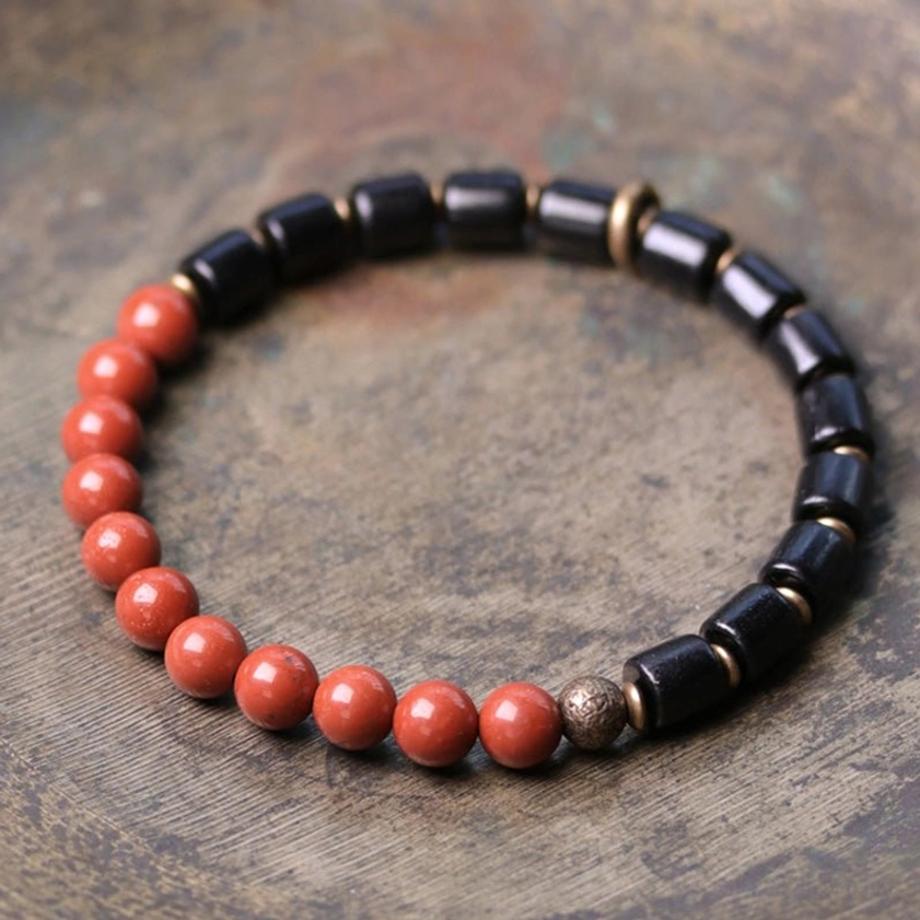 Ebony wood and red jasper Buddhist bracelet flat lay on rustic wooden surface showing natural gemstone beads and copper spacers