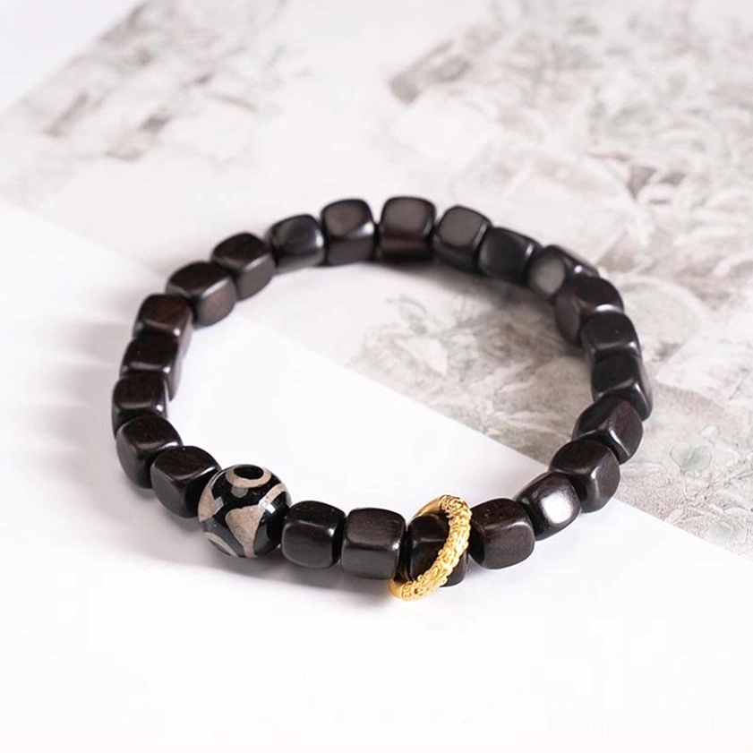 Round bead ebony wood dzi bracelet with nine-eye dzi ornament and gold metal ring detail on vintage printed paper background