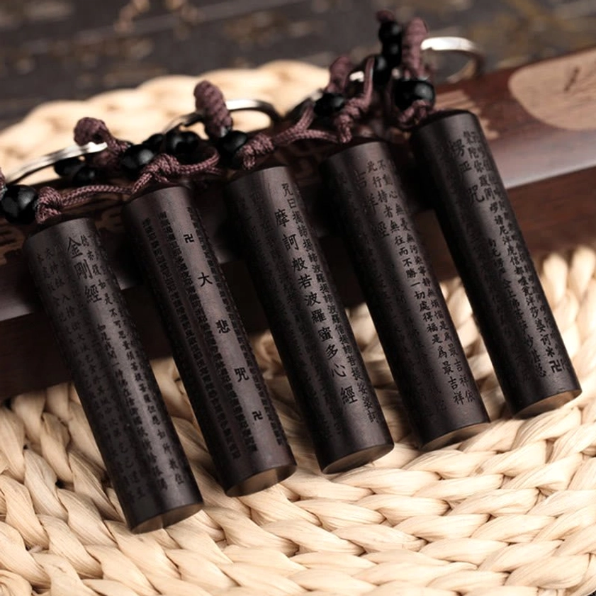 Multiple handcrafted ebony Heart Sutra keychains with different sutras engraved, arranged on woven mat showing collection variety