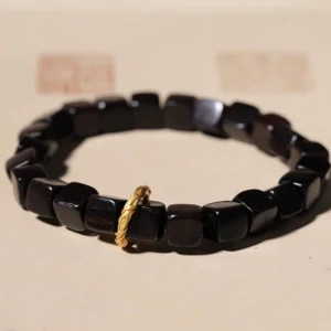 Ebony wood square bead bracelet with twisted copper clasp, overhead view on light beige surface with traditional seals