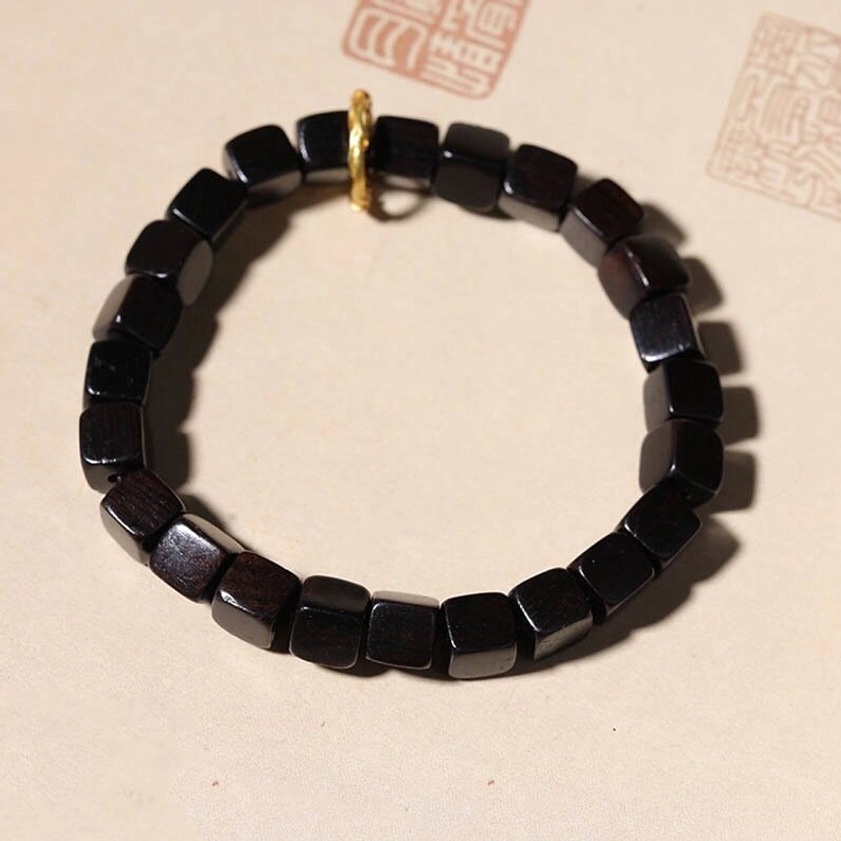 Uniform ebony wood square bead bracelet top-down view with gold decorative ring on antique Chinese seals