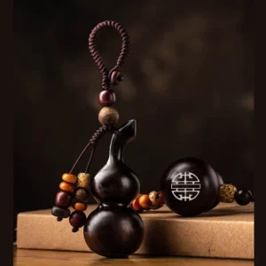 Handcrafted ebony vertical gourd Buddhist keychain with braided rope strap and double happiness engraving, displayed on kraft book desktop for spiritual protection