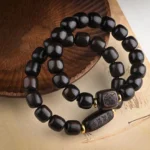 Dark ebony wood barrel bead bracelet with carved decorative accents and gold metal spacers on wooden coaster, flat lay view