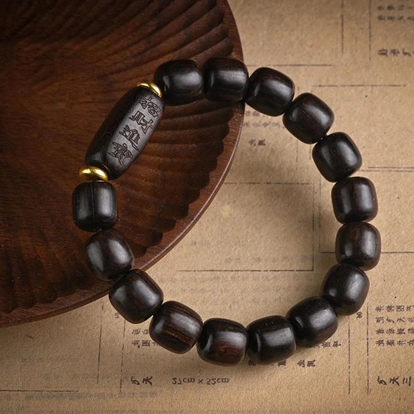 Handmade ebony wood barrel bead bracelet with carved long accent bead and gold spacer rings on vintage paper and wooden coaster
