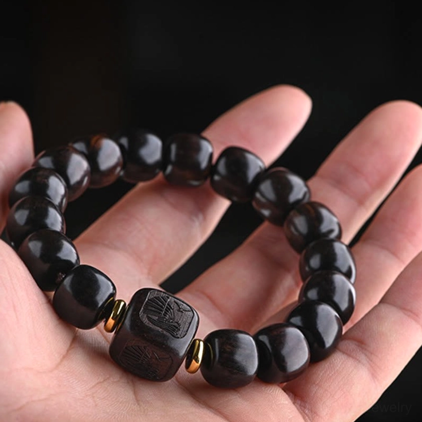 Side view of dark wood barrel bead bracelet with carved square bead and gold spacers on natural human palm pose