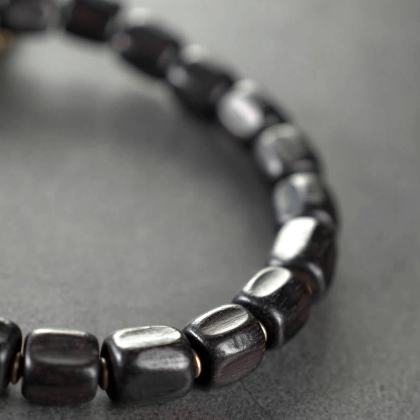 Close-up detail of matte black ebony wood cylindrical barrel beads on Buddhist healing bracelet