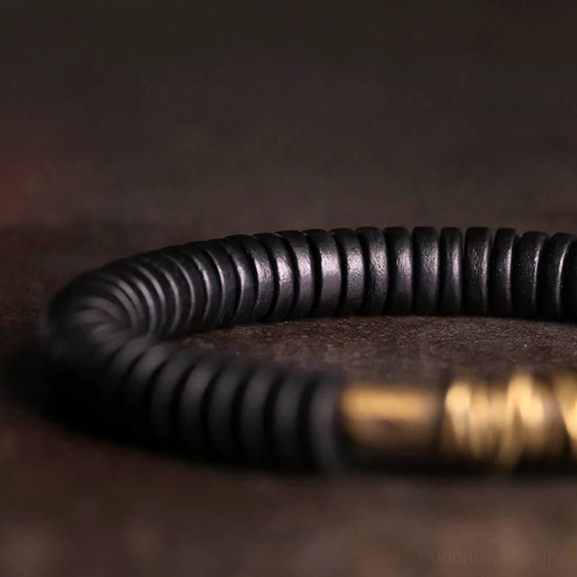 Close-up macro view of ebony wood bead texture and polished copper wrapped accent section of Buddhist bracelet