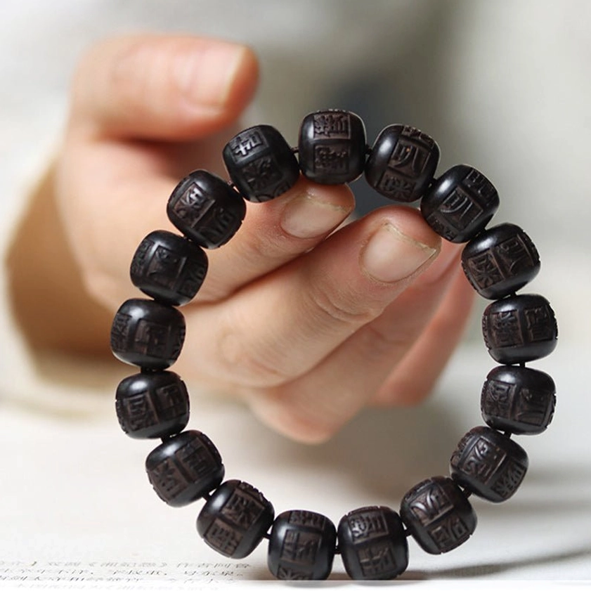 Close-up side view of ebony wood bracelet held between hands displaying intricate bead engraving