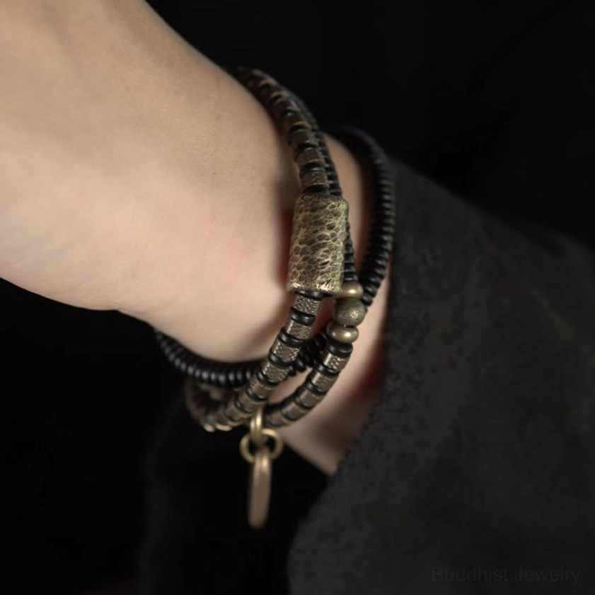 Single wrap ebony wood copper bracelet on human wrist with antique brass barrel bead and metal pendant charm