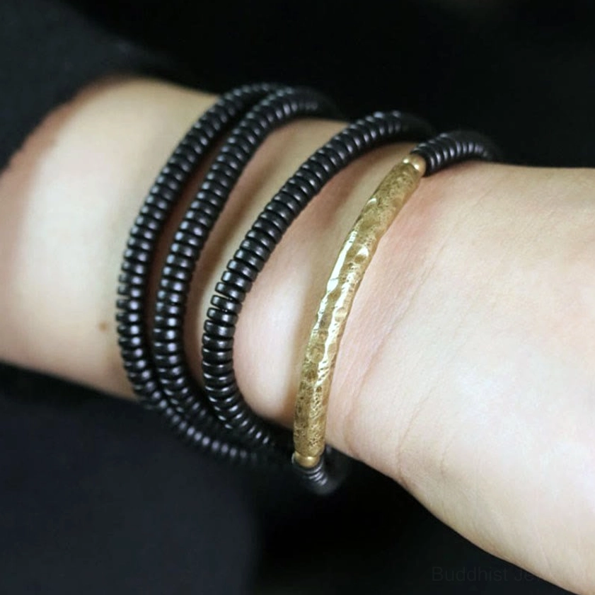 Side view of ebony and brass Buddhist bracelet stacked on wrist, showing aged hardware details