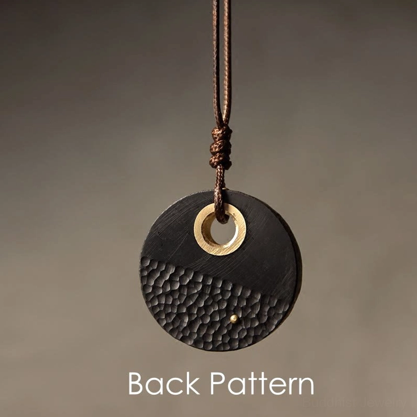 Back view of handcrafted Buddhist peace pendant showing brass hanging ring and carved rear pattern on ebony wood