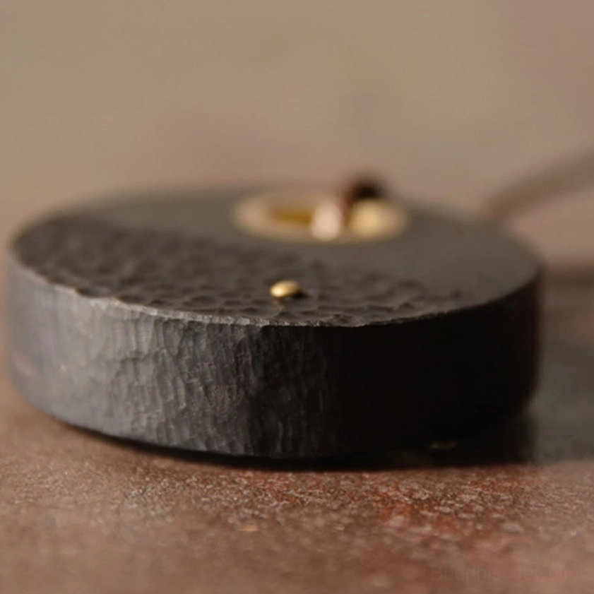 Close-up side view of handcrafted ebony wood pendant showing solid construction, hammered surface, and brass hardware detail
