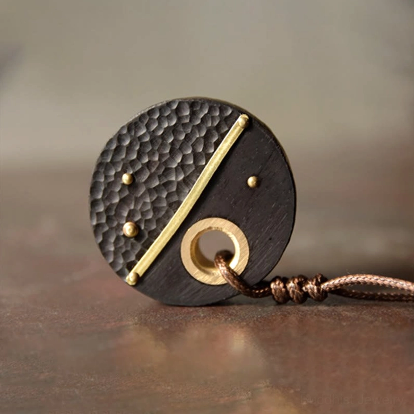 Front view of ebony wood and brass Buddhist peace pendant lying flat, displaying hammer texture and brass accents