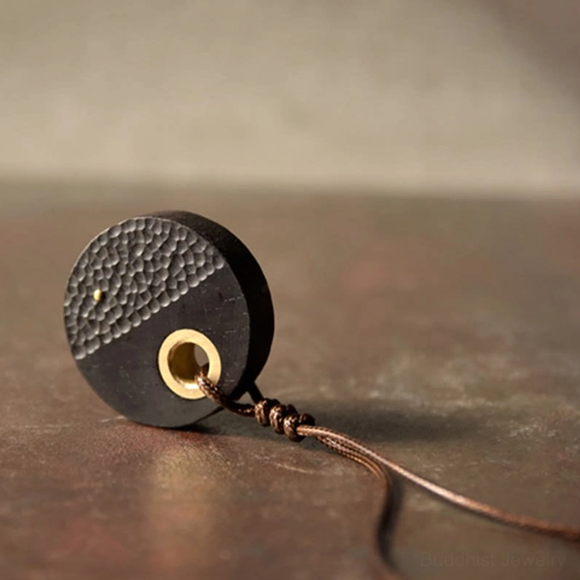 Loose ebony wood round pendant with brass ring and brown cord, showing hammered texture detail and craftsmanship