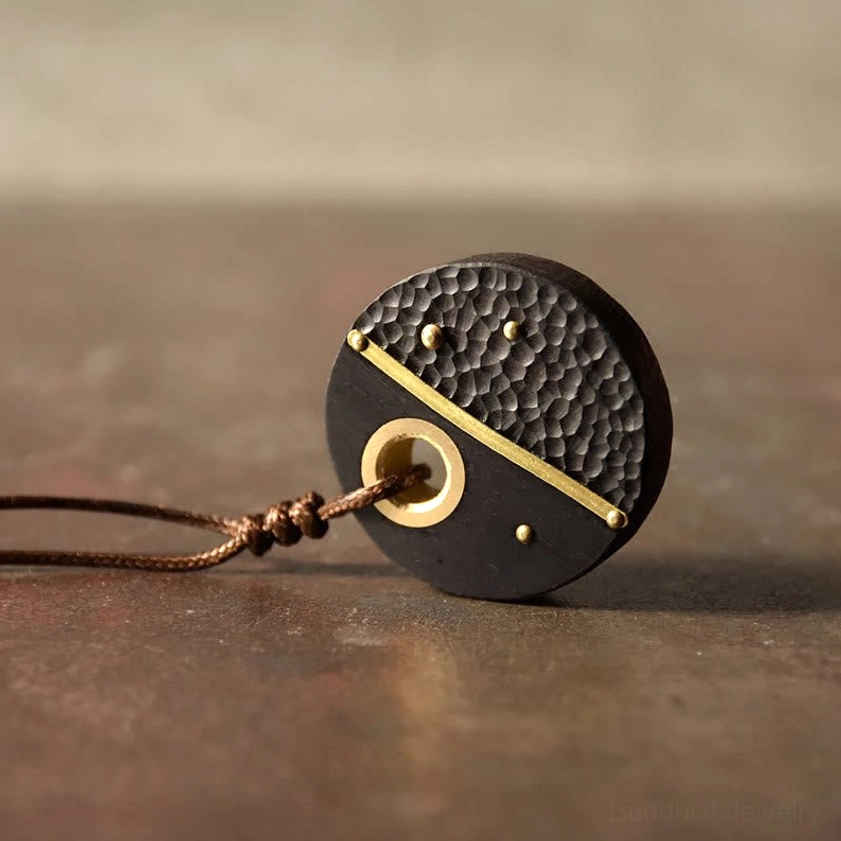 Side view of Buddhist peace necklace pendant lying flat, showing ebony wood, brass hardware, and natural wax rope