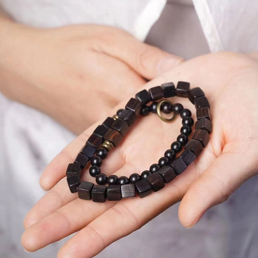 Ebony wood square beads double wrap Buddhist bracelet held in hand showing dark brown wood grain and mixed round square beads with copper metal clasp