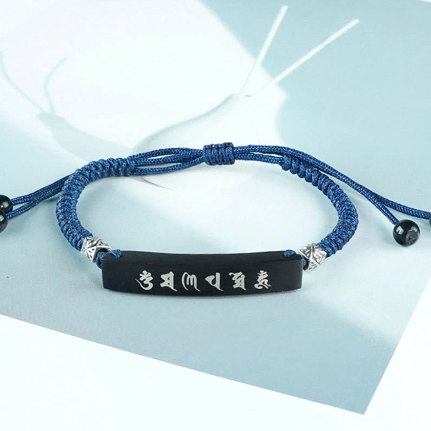 Complete ebony wood Buddhist bracelet flat lay with navy braided cord, black agate adjusters, and silver decorative parts on light blue and brown paper background