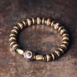Ebony wood bone beads Buddhist bracelet with central Dzi bead on dark rustic metal surface, showing intricate design and warm bronze tones
