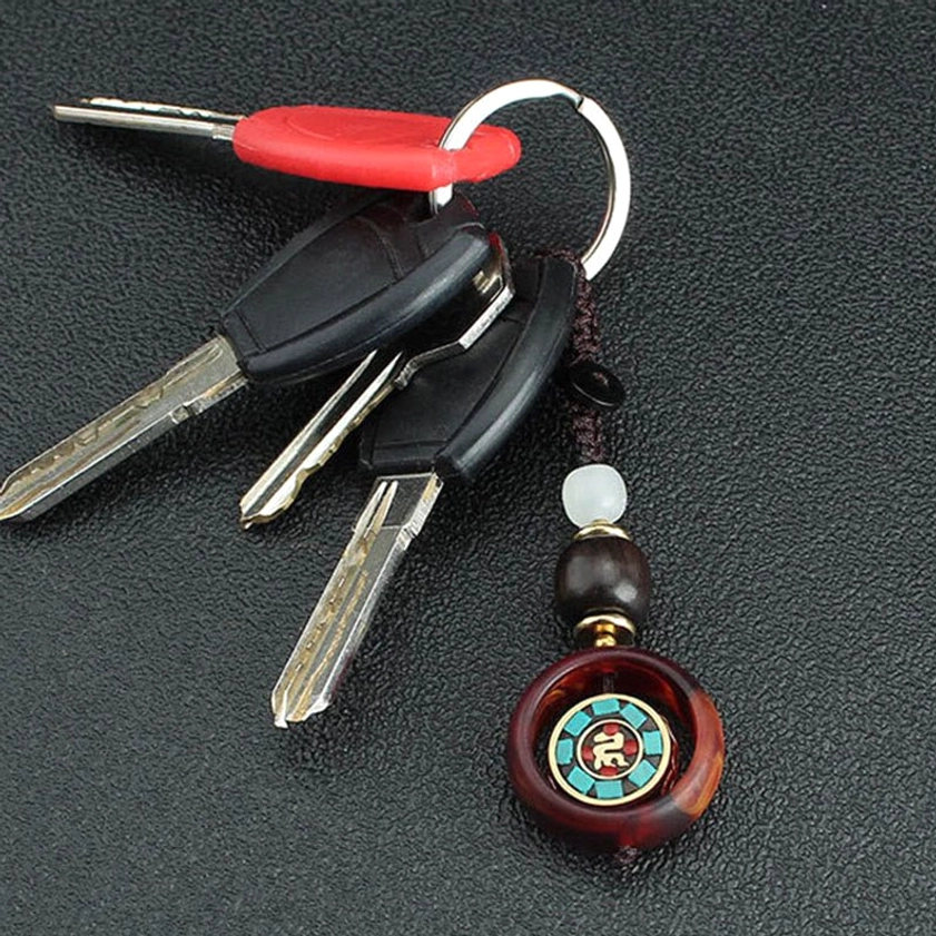 Rotatable Buddhist keychain attached to car keys with rotating Sanskrit emblem on textured black background
