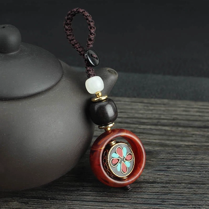 Side perspective of rotatable four-leaf clover Buddhist keychain with turquoise and red accents on wooden table setting