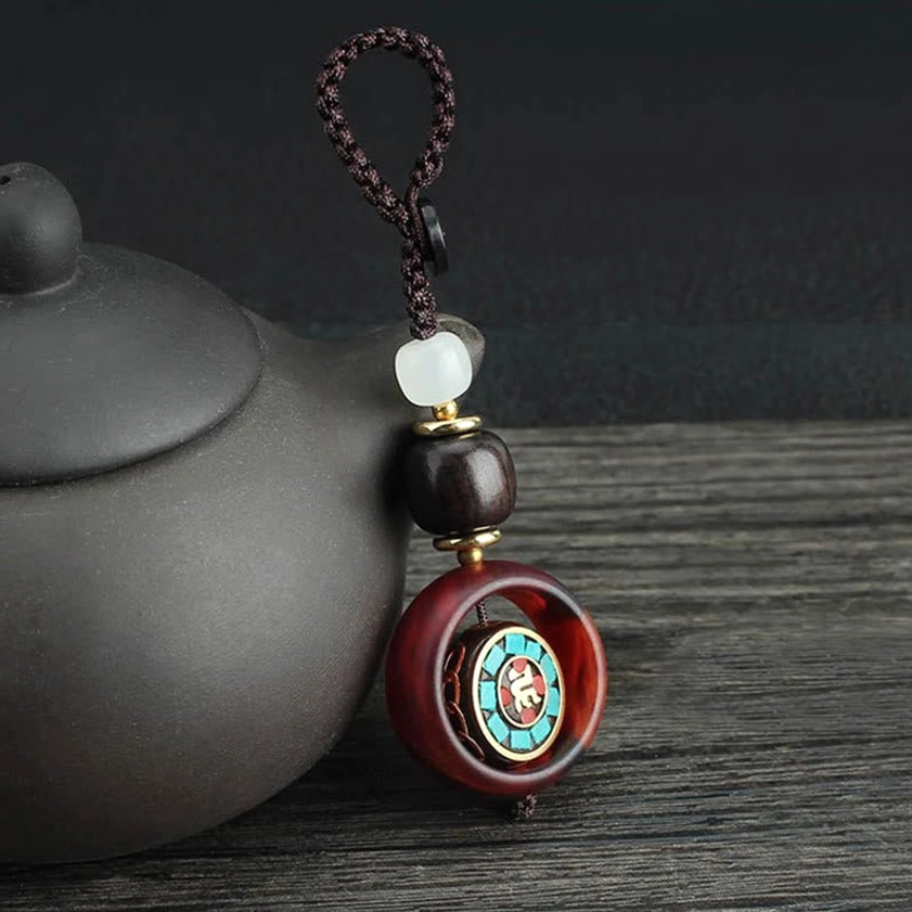 Ebony wood rotatable Sanskrit pattern Buddhist keychain displayed on wooden table with traditional teapot and spiritual ambiance