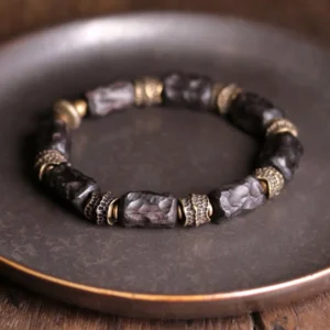 Ebony wood and copper Buddhist bracelet overhead flat lay view on bronze-rimmed plate