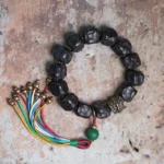 Ebony wood and copper Buddhist mala bracelet with multicolor silk tassel and green accent bead - flat lay view