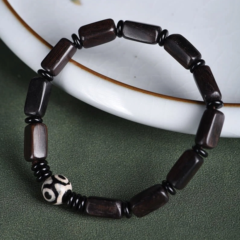 Overhead flat lay of ebony wood Dzi bead bracelet on minimalist green display, full circle view with polished beads
