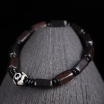 Ebony wood Dzi bead bracelet with two-eye design displayed on wooden stand, featuring polished dark rectangular beads and black spacers