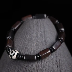 Ebony wood Dzi bead bracelet with two-eye design displayed on wooden stand, featuring polished dark rectangular beads and black spacers
