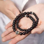Ebony wood dzi bead double wrap bracelet displayed in open hands overhead view showing two-strand design with dark wooden beads and protective dzi charm