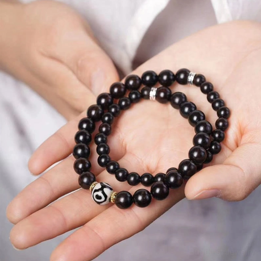 Ebony wood dzi bead double wrap bracelet displayed in open hands overhead view showing two-strand design with dark wooden beads and protective dzi charm