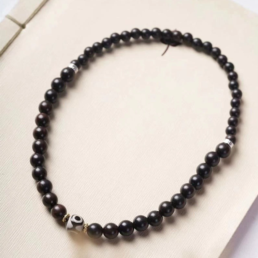Black ebony wood mala necklace with dzi bead and metal spacers flat lay on light paper background featuring continuous strand design