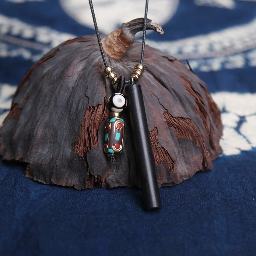 Close-up detail of ebony wood tube with white accent bead and patterned dzi charm on indigo fabric with dried lotus