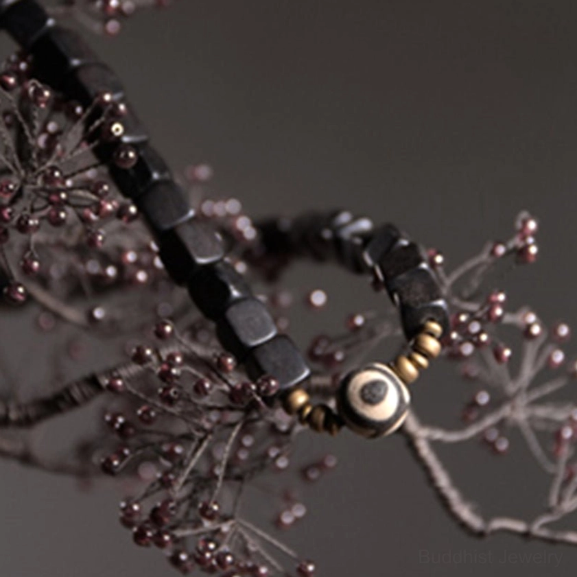 Single ebony wood dzi bead bracelet with gold spacers on botanical branch background
