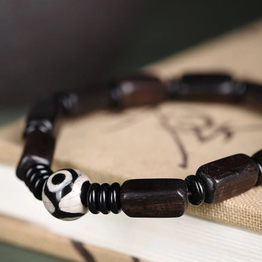 Side close-up view of ebony wood Buddhist bracelet showing matte dark beads and hand-painted two-eye Dzi accent bead