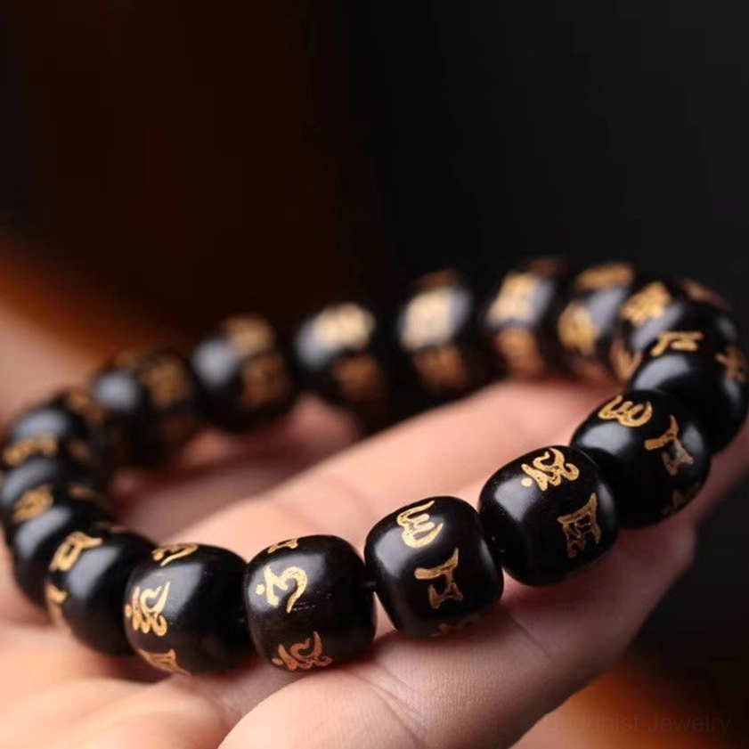 Black ebony wood mantra bracelet with golden carved Sanskrit, worn on human hand showing close-up detail of beads