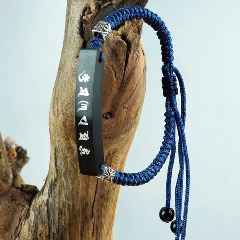 Ebony wood silver-inlaid Buddhist bracelet hanging vertically with long tassel cords and black agate bead adjusters on weathered wooden stump background