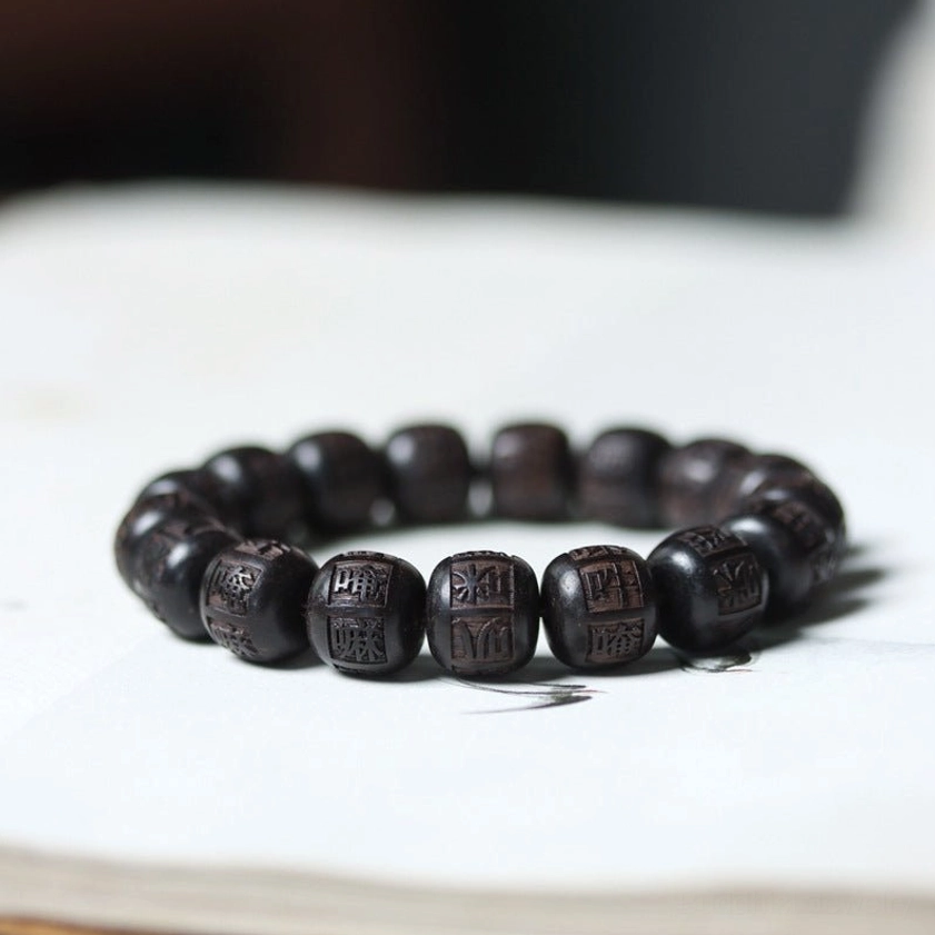 Ebony wood Om Mani Padme Hum engraved bracelet on book flat lay showing dark wooden beads with Sanskrit characters