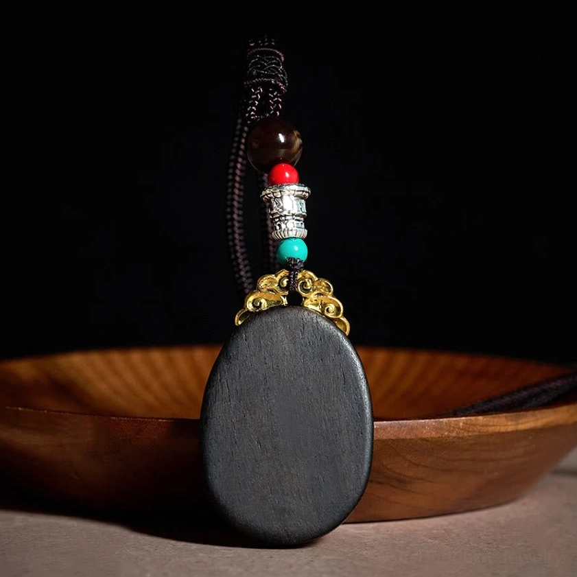 Back view of handmade ebony wood pendant necklace showing solid black backplate and woven rope chain construction