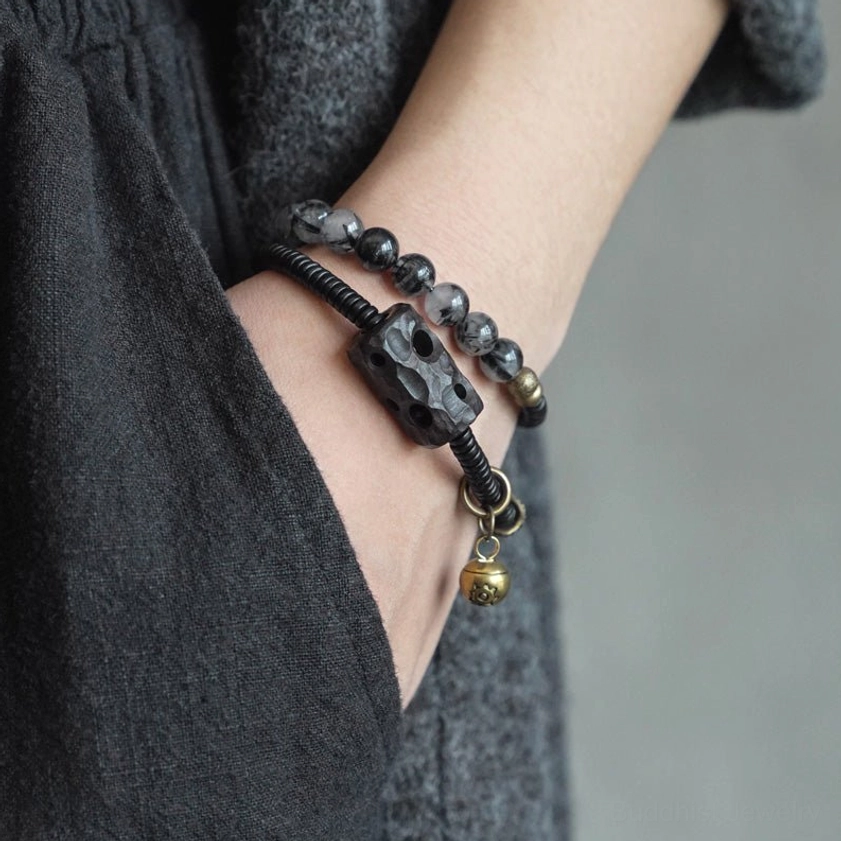 Handcrafted Buddhist couple bracelet worn on wrist with dark linen clothing background, showing double-layer design and metal pendant